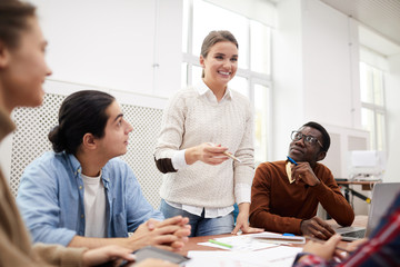 Multi-ethnic group of students working together on team project while studying in college, focus on smiling girl heading meeting