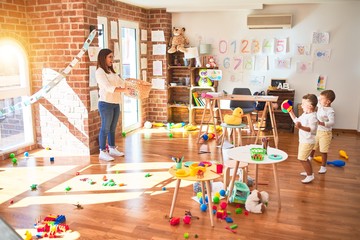 Beautiful teacher and toddlers playing basketball using balls and wicker basket  around lots of toys at kindergarten