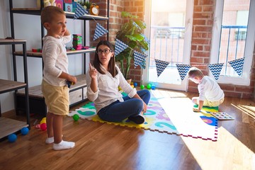 Beautiful teacher angry poiting with finger to toddler around lots of toys at kindergarten