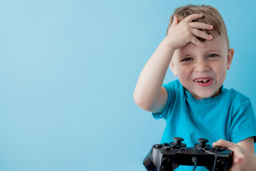 Little kid boy 2-3 years old wearing blue clothes hold in hand joystick for gameson blue background children studio portrait. People childhood lifestyle concept. Mock up copy space