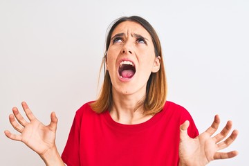 Beautiful redhead woman wearing casual red t-shirt over isolated background crazy and mad shouting and yelling with aggressive expression and arms raised. Frustration concept.