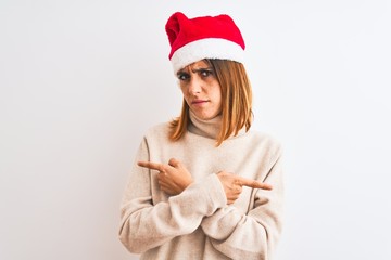 Beautiful redhead woman wearing christmas hat over isolated background Pointing to both sides with fingers, different direction disagree