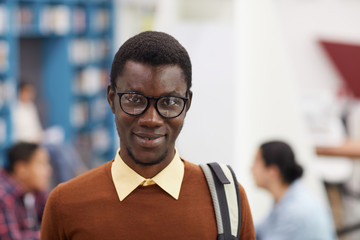 Obraz premium Head and shoulders portrait of smiling African-American student looking at camera while standing in library of modern college, copy space