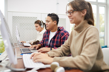 Side view at students using computers sitting in row while studying on college library, copy space