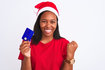 Young african american woman wearing christmas hat and holding credit card screaming proud and celebrating victory and success very excited, cheering emotion