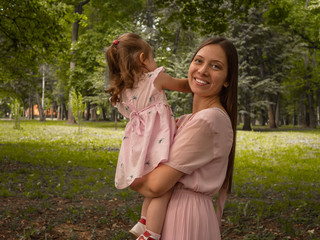 Mom and daughter walk and play in the park. Dressed in dresses. Sunny day, weekend in a city park.