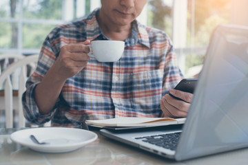 Man using smart phone and working on laptop computer in cafe