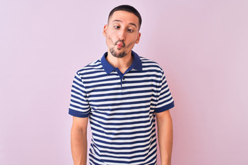Young handsome man wearing nautical striped t-shirt over pink isolated background making fish face with lips, crazy and comical gesture. Funny expression.