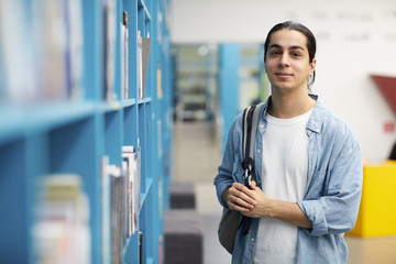 Fototapeta Waist up portrait of Latin-American student looking at camera while standing by shelves in college library, copy space obraz