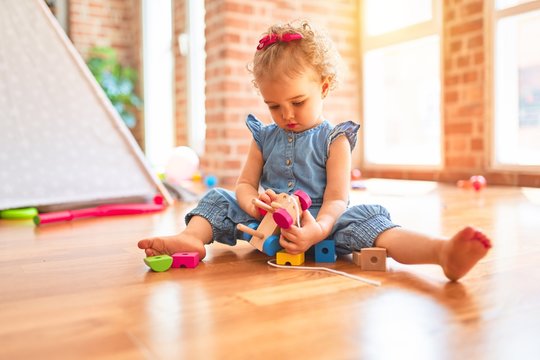 Beautiful caucasian infant playing with toys at colorful playroom. Happy and playful with wooden train pieces at kindergarten.