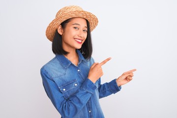 Young beautiful chinese woman wearing denim shirt and hat over isolated white background smiling and looking at the camera pointing with two hands and fingers to the side.