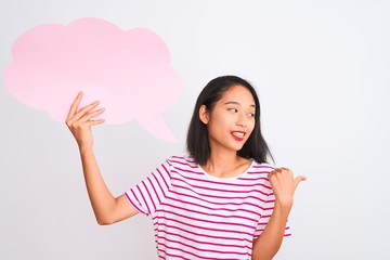 Young chinese woman holding cloud speech bubble standing over isolated white background pointing and showing with thumb up to the side with happy face smiling