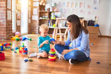 Young caucasian child playing at playschool with teacher. Mother and son at playroom with intelligence toy