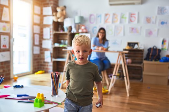 Young caucasian child playing at playschool with teacher. Young woman sitting on the desk of the classroom