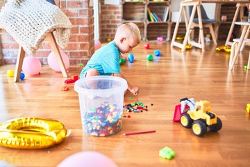 Young caucasian kid playing at kindergarten with toys. Preschooler boy happy at playroom.