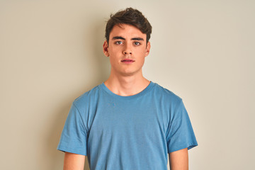 Teenager boy wearing casual t-shirt standing over isolated background with serious expression on face. Simple and natural looking at the camera. - obrazy, fototapety, plakaty