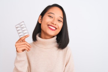 Young beautiful chinese woman holding pills standing over isolated white background with a happy face standing and smiling with a confident smile showing teeth