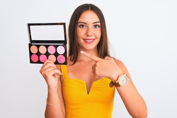 Young beautiful girl holding makeup standing over isolated white background very happy pointing with hand and finger