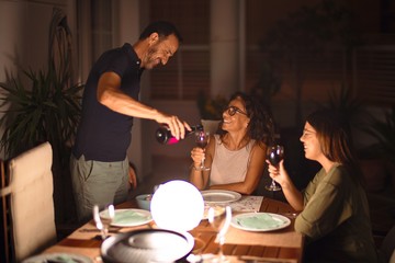 Beautiful family dinning, drinking cup of wine smiling at terrace