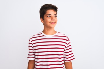 Handsome teenager boy standing over white isolated background looking away to side with smile on...