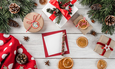 Creative layout frame made of Christmas tree branches, paper card note, pine cones, gifts, Christmas sweater on white wooden background. Xmas and New Year theme. Flat lay, top view