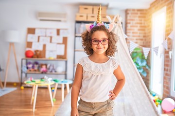 Beautiful toddler wearing glasses and unicorn diadem standing and smiling at kindergarten