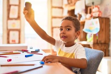 Beautiful african american toddler sitting on desk playing with cars at kindergarten