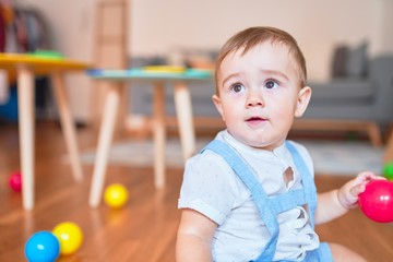 Beautiful toddler sitting on the floor playing with small colorful balls at kindergarten