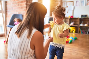 Young beautiful teacher and toddler playing with small building blocks toy at kindergarten