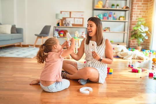 Young beautiful teacher teaching alphabet to blond student toddler girl at kindergarten