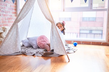 Beautiful toddler girl sitting on the floor playing with unicorn inside tipi at kindergarten © Krakenimages.com