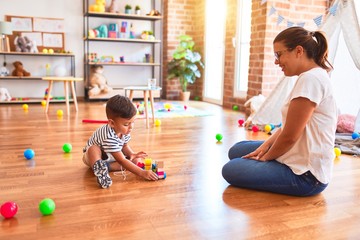 Fototapeta premium Beautiful teacher and toddler boy playing with train at kindergarten