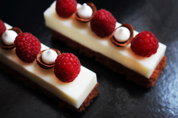 White mousse desserts with raspberries and meringues on brownie base top view