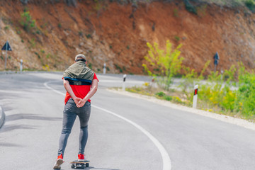 Fototapeta premium Tall athlete riding his longboard fast and steady downhill while wearing red t-shirt and black jeans.