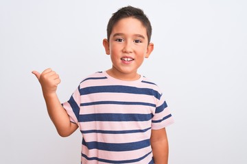 Beautiful kid boy wearing casual striped t-shirt standing over isolated white background smiling with happy face looking and pointing to the side with thumb up.