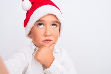 Beautiful kid boy wearing Christmas Santa hat make selfie over isolated white background serious face thinking about question, very confused idea