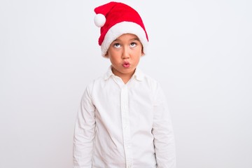 Beautiful kid boy wearing Christmas Santa hat standing over isolated white background making fish face with lips, crazy and comical gesture. Funny expression.