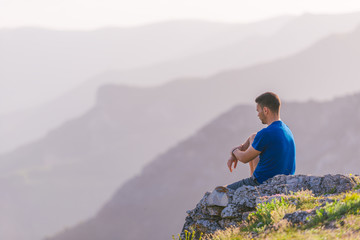 Naklejka premium Adventurous man sitting on top of a mountain and enjoying the beautiful view, while looking downhill at the blue river and amazing mountain line..