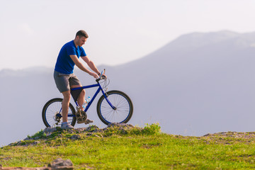 Fototapeta premium Fit mountain biker riding his bike through green grass on top of a mountain.
