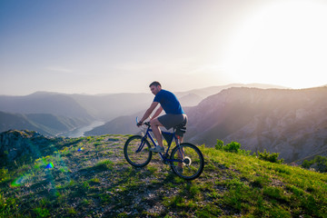 Fototapeta premium Adventurous Cyclist riding his mountain bike at the edge of a cliff, on rocky terrain while wearing no safety equipment.Amazing top view.