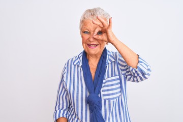 Senior grey-haired woman wearing blue striped shirt standing over isolated white background doing ok gesture with hand smiling, eye looking through fingers with happy face.