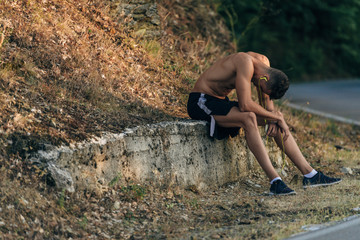 Portrait of a tired sportsman resting after workout at the mountain, listening to music with earphones