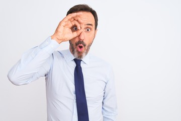 Middle age businessman wearing elegant tie standing over isolated white background doing ok gesture shocked with surprised face, eye looking through fingers. Unbelieving expression.