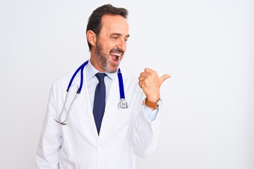 Middle age doctor man wearing coat and stethoscope standing over isolated white background smiling with happy face looking and pointing to the side with thumb up.