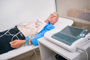 Doctor ( cardiologist ) is attaching vacuum sensors to an elder ( senior )patient for recording ECG...