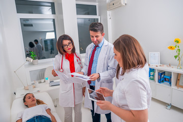 Group of doctors standing next to a sick patient and discussing the causes for his sickness.