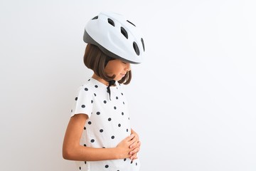 Beautiful child girl wearing security bike helmet standing over isolated white background with hand on stomach because nausea, painful disease feeling unwell. Ache concept.