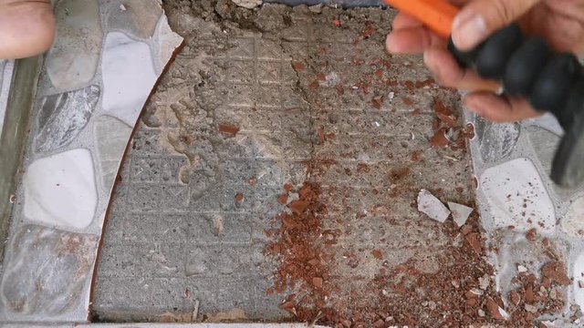 club hammer hitting a bolster chisel, to loosen a piece of tile fixed to a floor.