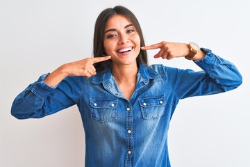Young beautiful woman wearing casual denim shirt standing over isolated white background smiling cheerful showing and pointing with fingers teeth and mouth. Dental health concept.