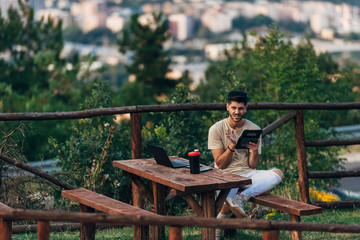 Fototapeta premium Photo of smiling emotional young bearded man outdoors using digital tablet